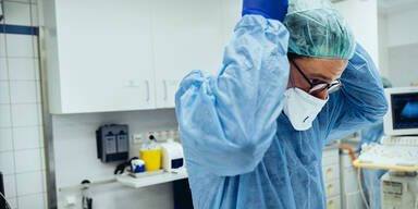 Arzt im Schutzanzug setzt im OP FFP2-Maske auf