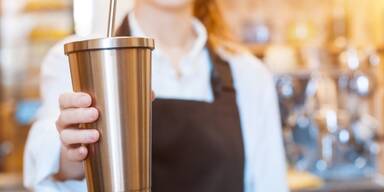 Barista hält To Go Kaffeebecher mit Strohhalm