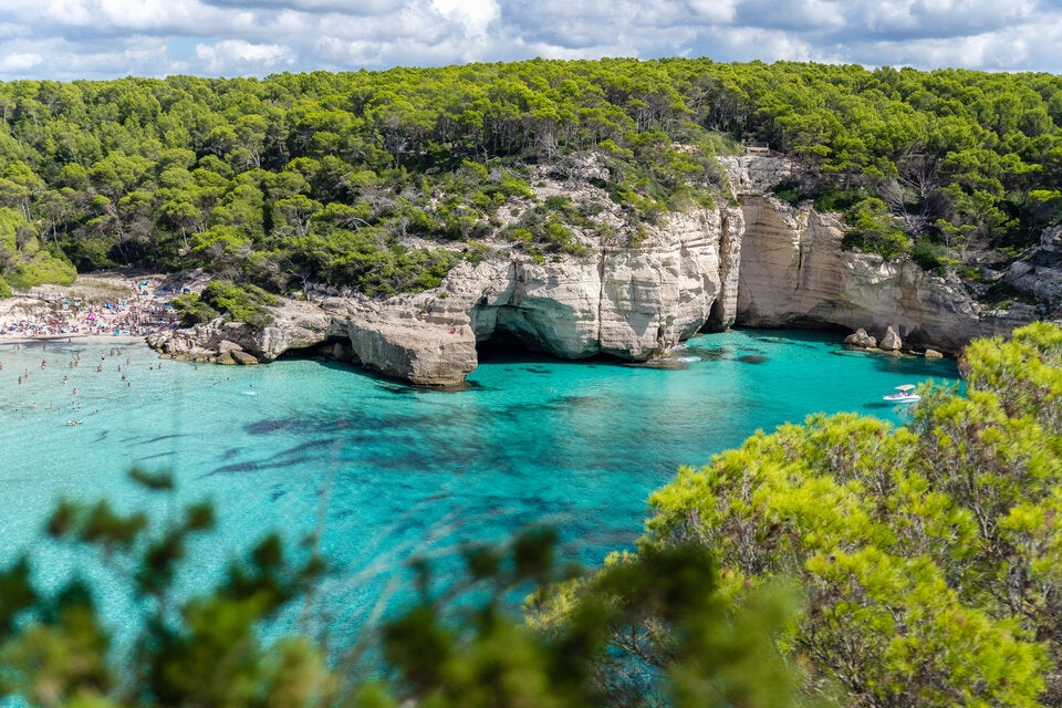Cala Mitjana, ein feinkörniger Sandstrand, der von Felsen und Bäumen umgeben ist.