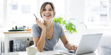 Gl&uuml;ckliche Frau am Schreibtisch im Heimb&uuml;ro