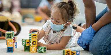 Kindergartenkind spielt mit Blöcken und trägt Maske