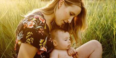 Mutter sitzt mit Kind auf einer gr&uuml;nen Wiese.