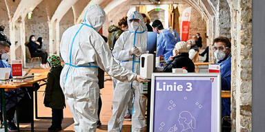 Menschen in Schutzanz&uuml;gen in einer Corona-Teststra&szlig;e