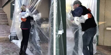 Trauernde umarmen sich durch Plastik-Vorhang