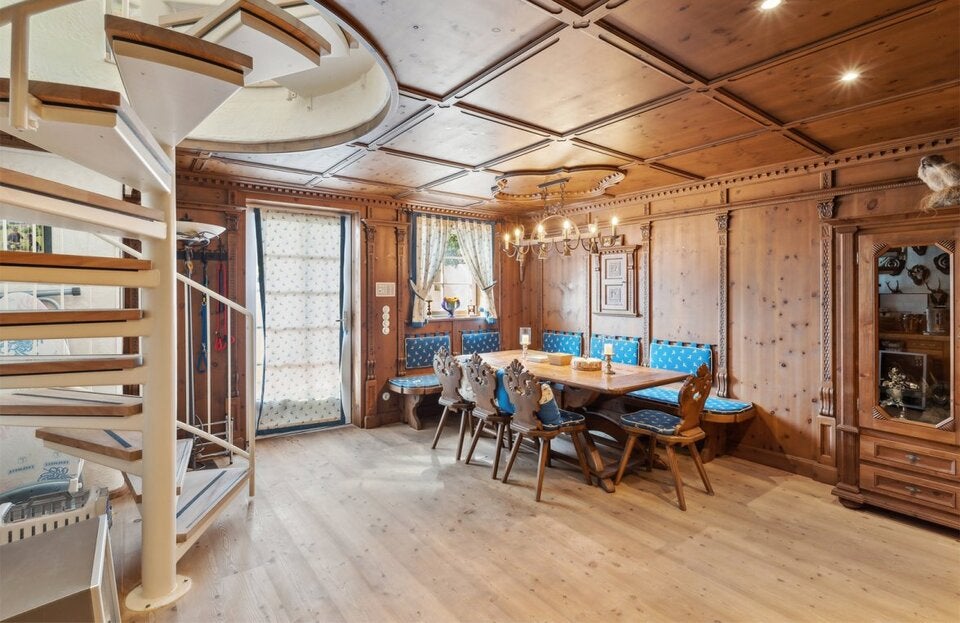 Uriger Treffpunkt in der gemütlichen Stube: Der mit Holz ausgekleidete Raum mit in einer Vitrine ausgestellten Jagdtrophäen ist ein rustikaler Gegenpol zu dem modernen Ambiente des Hauses. Blaue Sitzpolster bringen ein bisschen Farbe hinein. Die geschickt verteilte Beleuchtung verhindert, dass es düster wirkt.