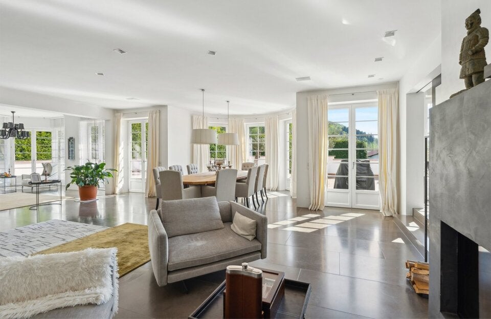 Wohlfühlraum im Wohnzimmer: Dank der raumhohen Fenster gelangt viel Sonnenlicht in den großzügigen Familienbereich. Das offene Raumkonzept vereint den Essbereich und eine Sitzecke vor dem modernen Kamin.