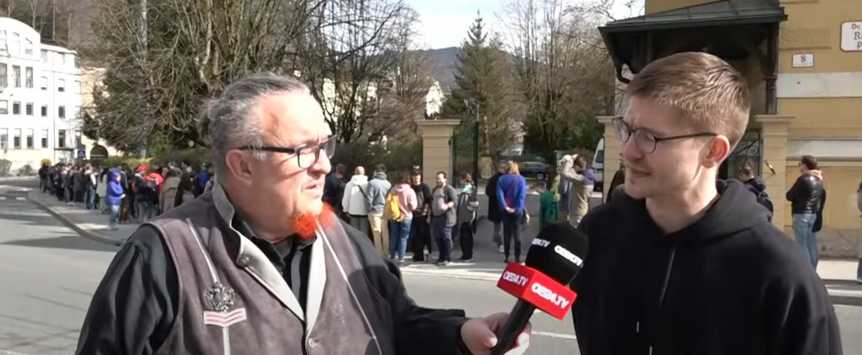 oe24.TV-Reporter Mike Vogl in Salzburg - im Hintergrund lange Warteschlange.