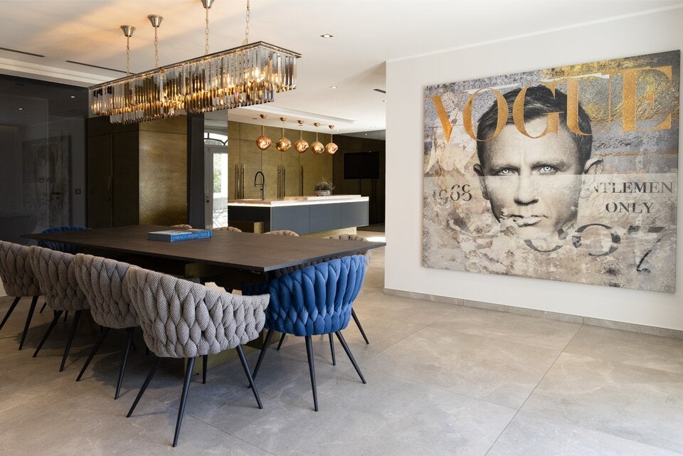 Die riesige Küche im Louis Vuitton-Style mündet direkt in den Essbereich mit Designermöbeln, funkelndem Luster und einem Bild von Daniel Craig alias James Bond.
